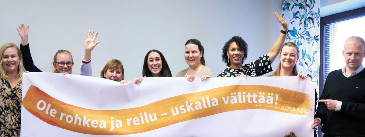 Ryhmäkuva moninaisuuskoulutuksesta. Ryhmä pitelee kylttiä, jossa on Yhteiset Lapsemme ry:n logo.