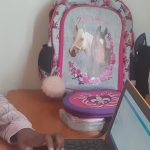 Tummaihoinen tyttö työpöydän ääressä ja katsoo kannettavan tietokoneen näyttöä.