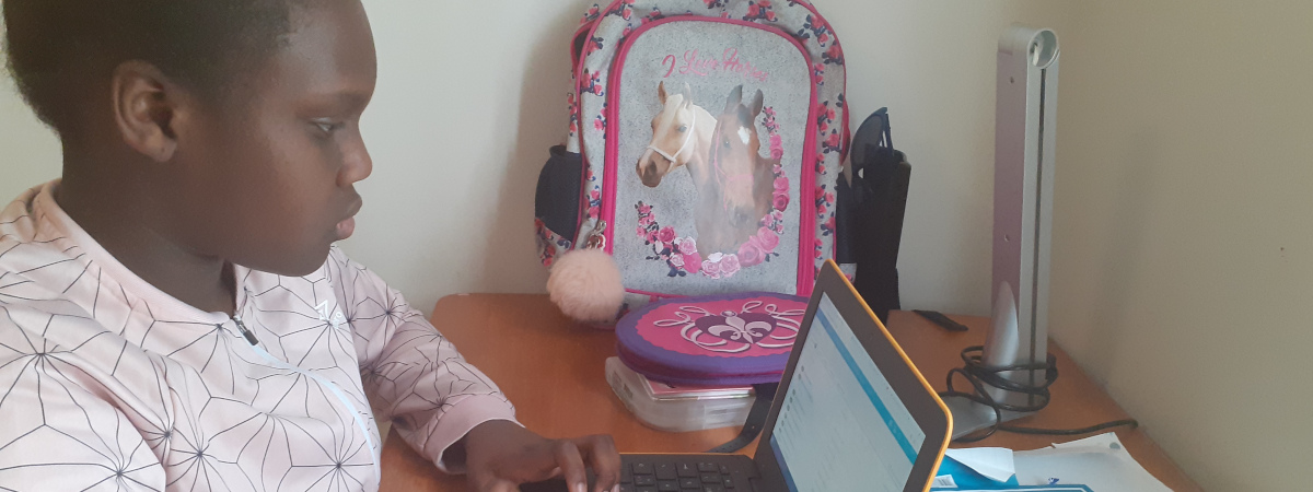 Tummaihoinen tyttö työpöydän ääressä ja katsoo kannettavan tietokoneen näyttöä.