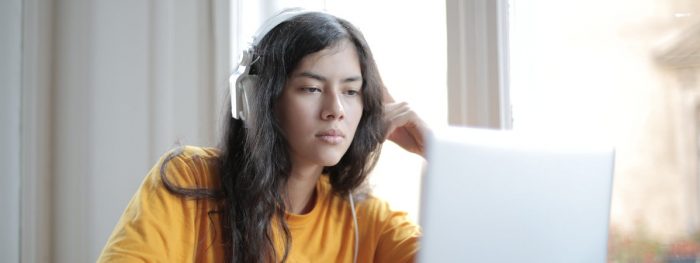 Keltapaitainen tyttö kuulokkeet korvillaan tietokoneen ääressä.