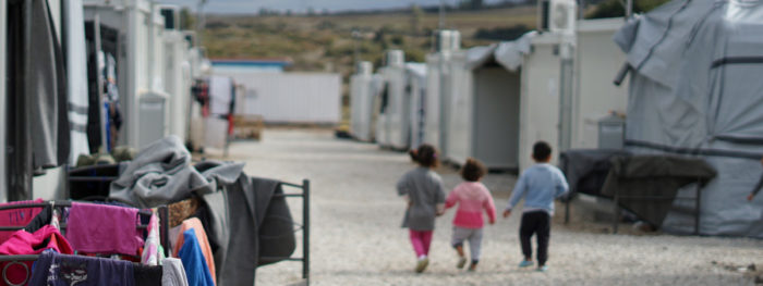 Kolme lasta kävelevät vierekkäin pakolaisleirillä.