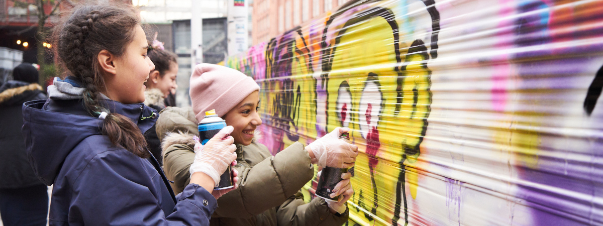 Kaksi tyttöä maalaa graffitiseinää.