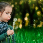 Lapsi puhaltaa voikukkaa vehreässä ympäristössä